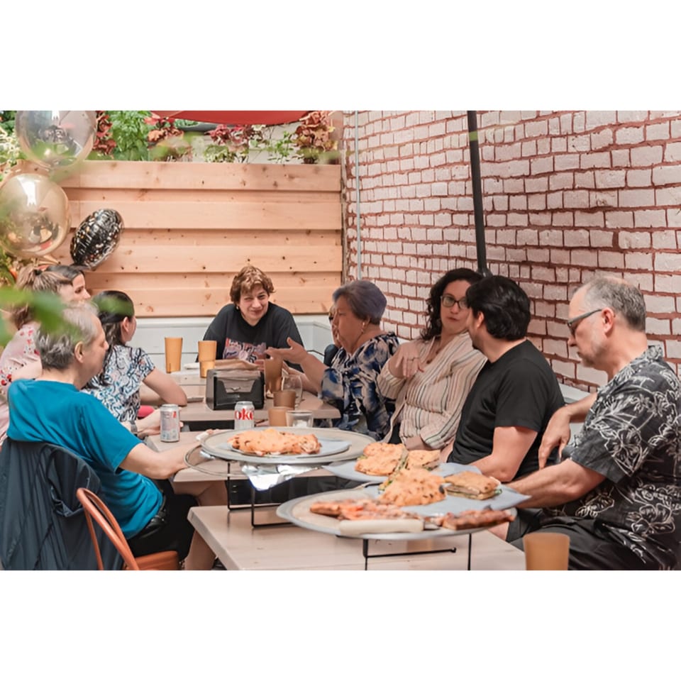 Diverse group of people enjoying pizza and conversation at an outdoor table at Brooklyn DOP FastLife.