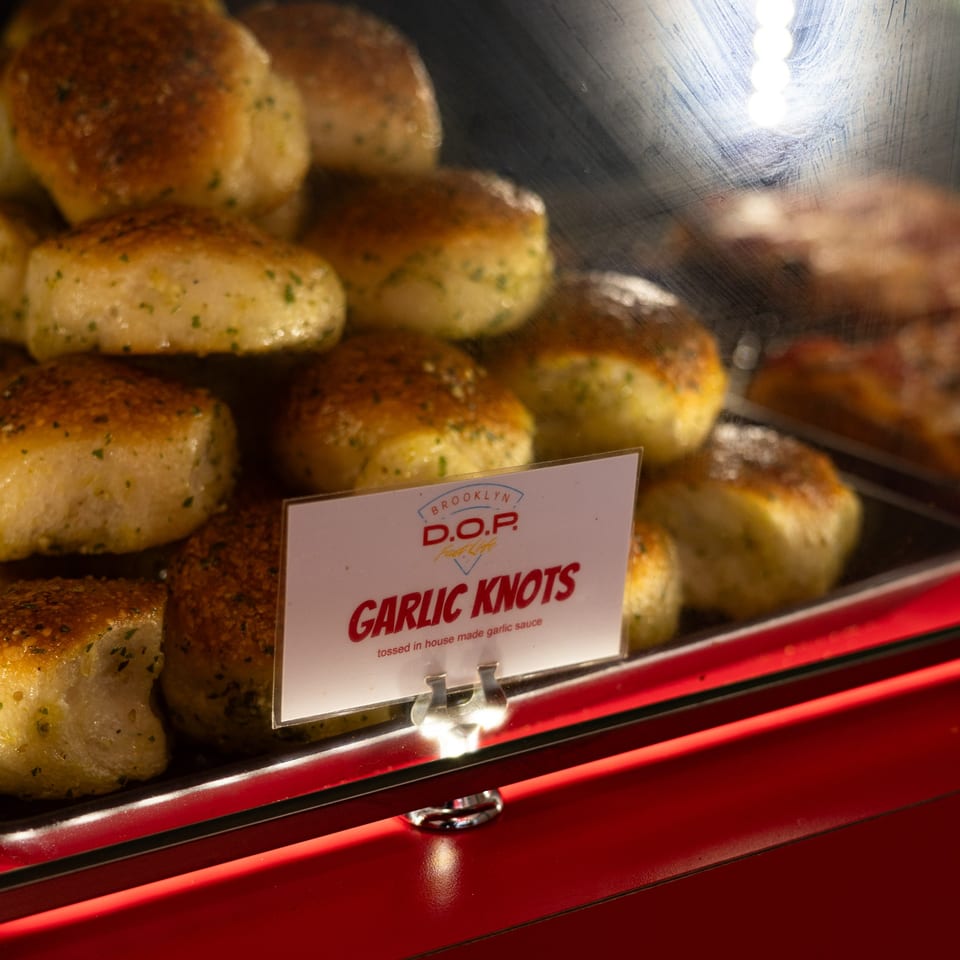 Golden-brown garlic knots with herbs, displayed in a glass case with a "Garlic Knots" sign.