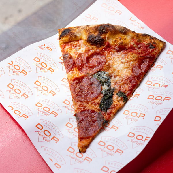 A single slice of Brooklyn DOP FastLife pepperoni pizza with a crispy crust on branded paper.