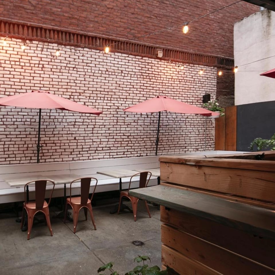 Outdoor patio at Brooklyn DOP FastLife with brick walls, string lights, orange umbrellas, and seating.