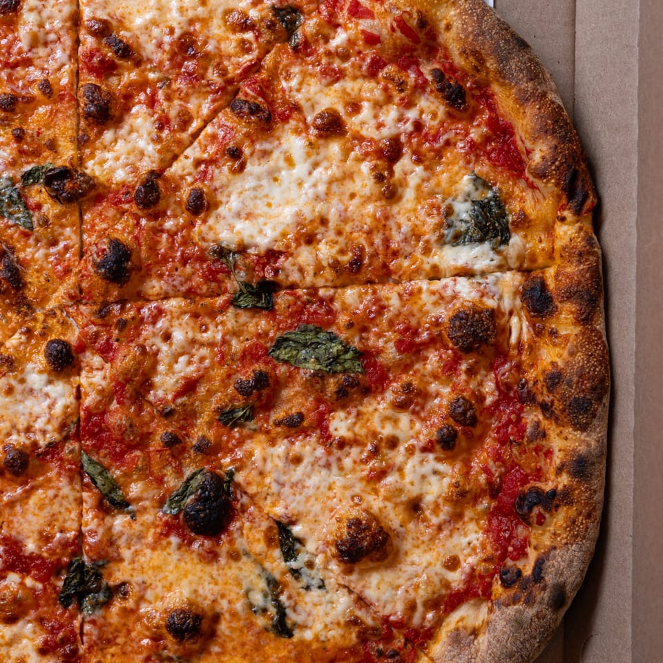 Close-up of a Brooklyn DOP FastLife pizza with melted cheese, tomato sauce, and basil in a box.